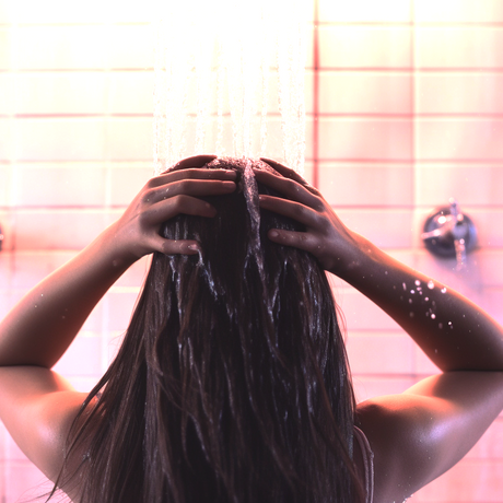 Picture of a woman showering her hair using municipal water. A depiction of how hard water causes hair loss without you even realizing it.