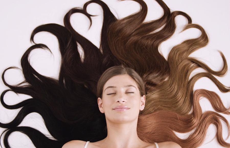 woman lying down with halo hair extensions. Hair is long and growth is due to knowing which oil is best for hair growth and thickness