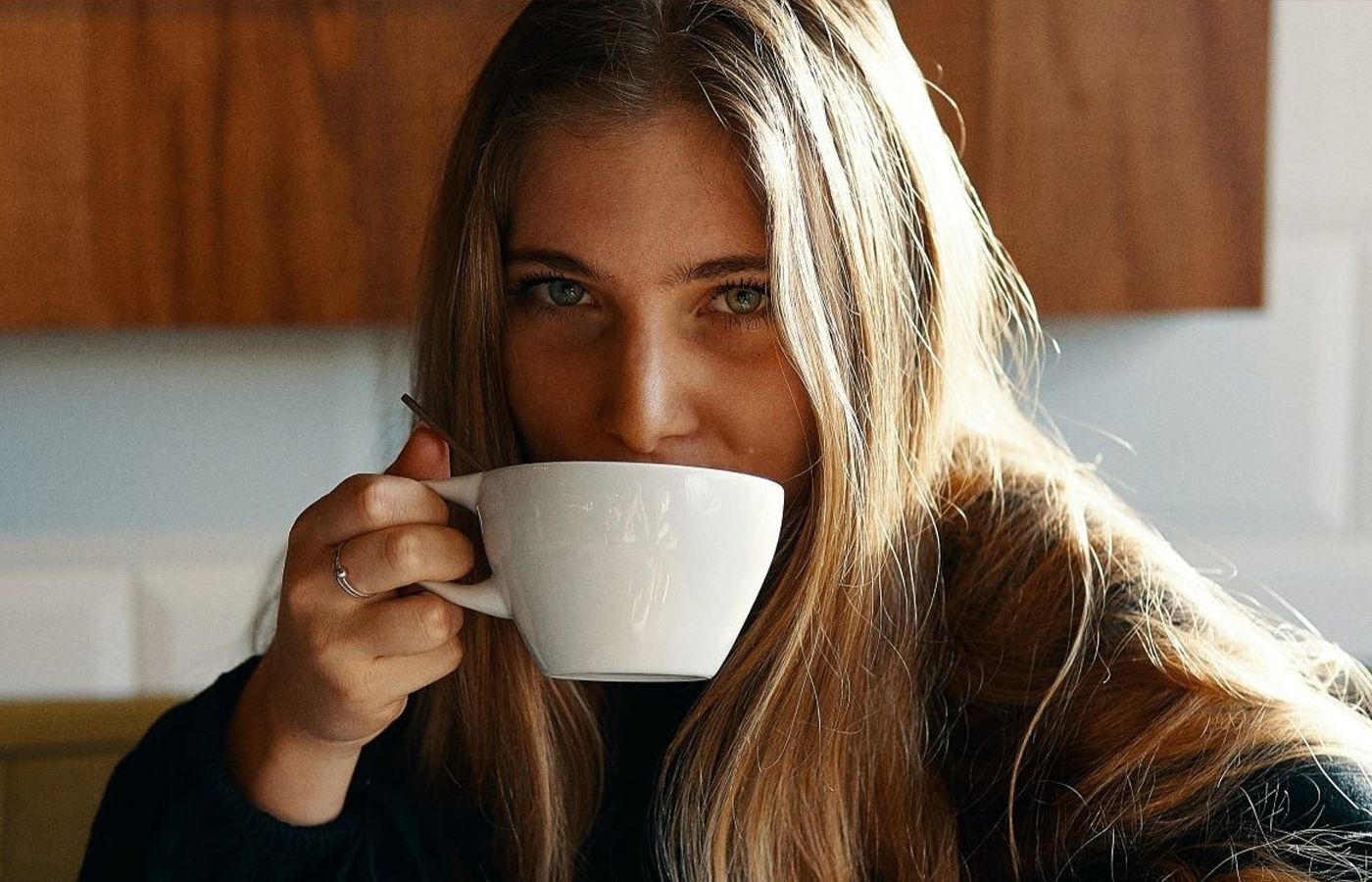 A young woman, sitting comfortably with a warm cup of coffee in hand, appears lost in thought as she contemplates the idea of a DIY coffee hair growth treatment.