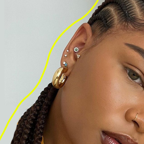 black woman with fulani braids and several ear piercings photographed from profile against a grey background