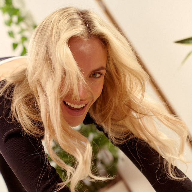 A smiling woman wears her halo hair extension while doing yoga