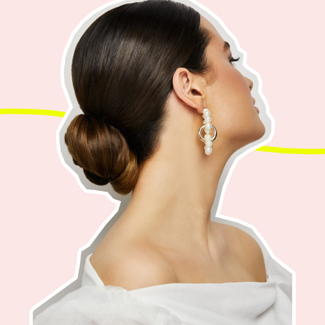 side profile photo of woman with formal hairstyle: low bun with slicked back roots; image is against pink background