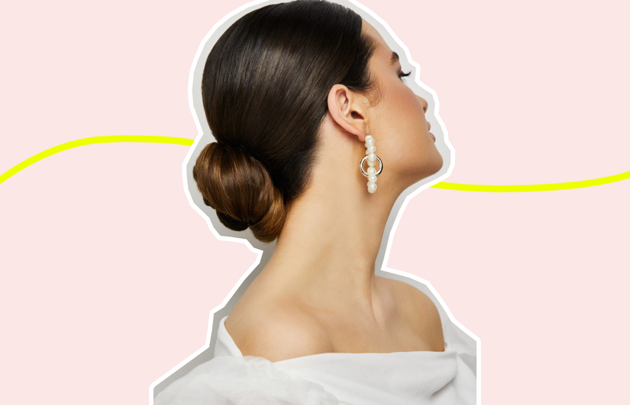 side profile photo of woman with formal hairstyle: low bun with slicked back roots; image is against pink background