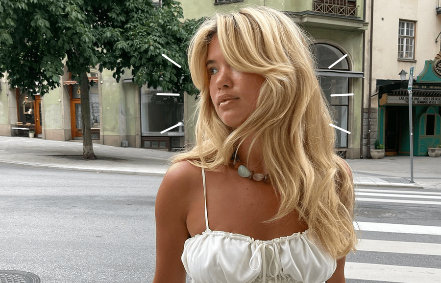 Blonde woman standing outside a hair salon, with a blend in hair technique performed on her hair.