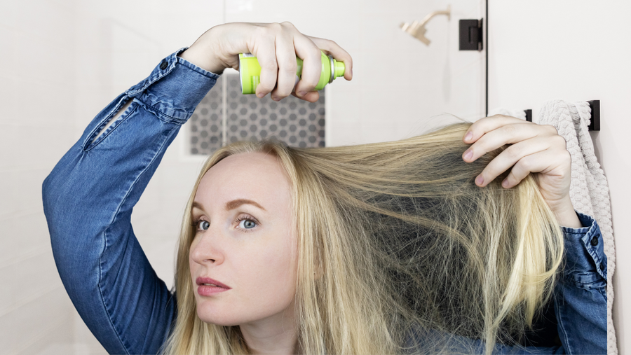 woman using a diy dry shampoo on her hair in front of a mirror