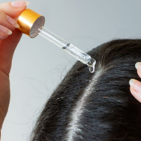 Woman applying Natural Oil to Hair with glass dropper; image is of scalp close up