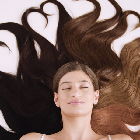 woman lying down with halo hair extensions. Hair is long and growth is due to knowing which oil is best for hair growth and thickness