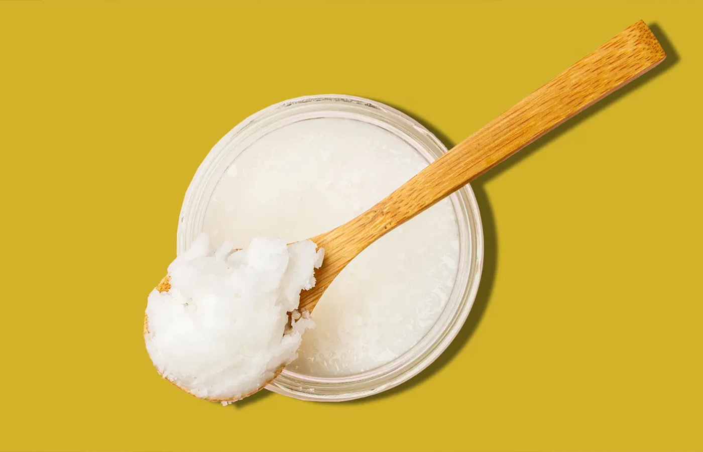 cup of coconut oil on yellow background; model off frame using benefits of coconut oil on skin