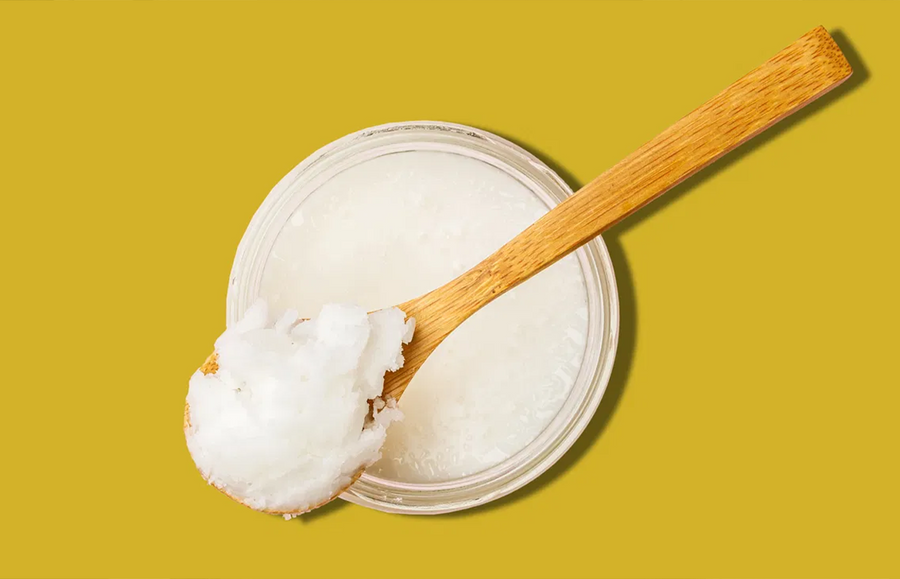 cup of coconut oil on yellow background; model off frame using benefits of coconut oil on skin