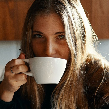 A young woman, sitting comfortably with a warm cup of coffee in hand, appears lost in thought as she contemplates the idea of a DIY coffee hair growth treatment.