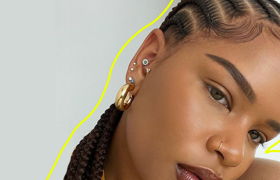 black woman with fulani braids and several ear piercings photographed from profile against a grey background