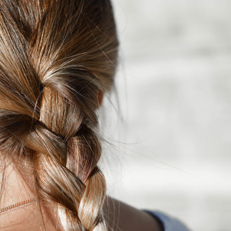 Naturally thicker fuller hair tied up in a plait. Photo taken from the back. Dark blonde hair colour.
