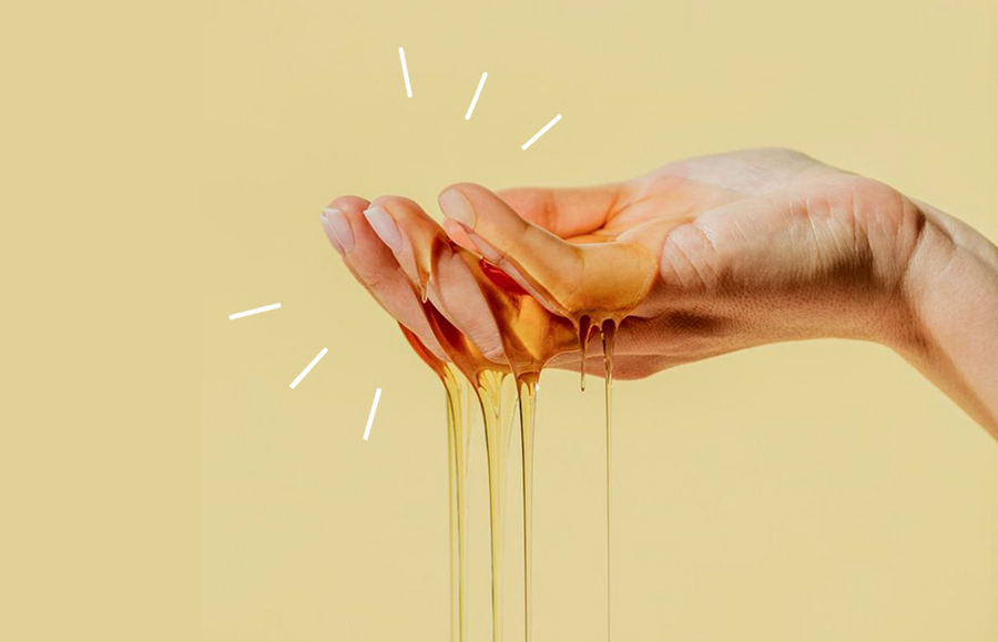 hand holding up sugaring paste created to remove body hair. hand is against yellow background. sugaring mixture is dark yellow.