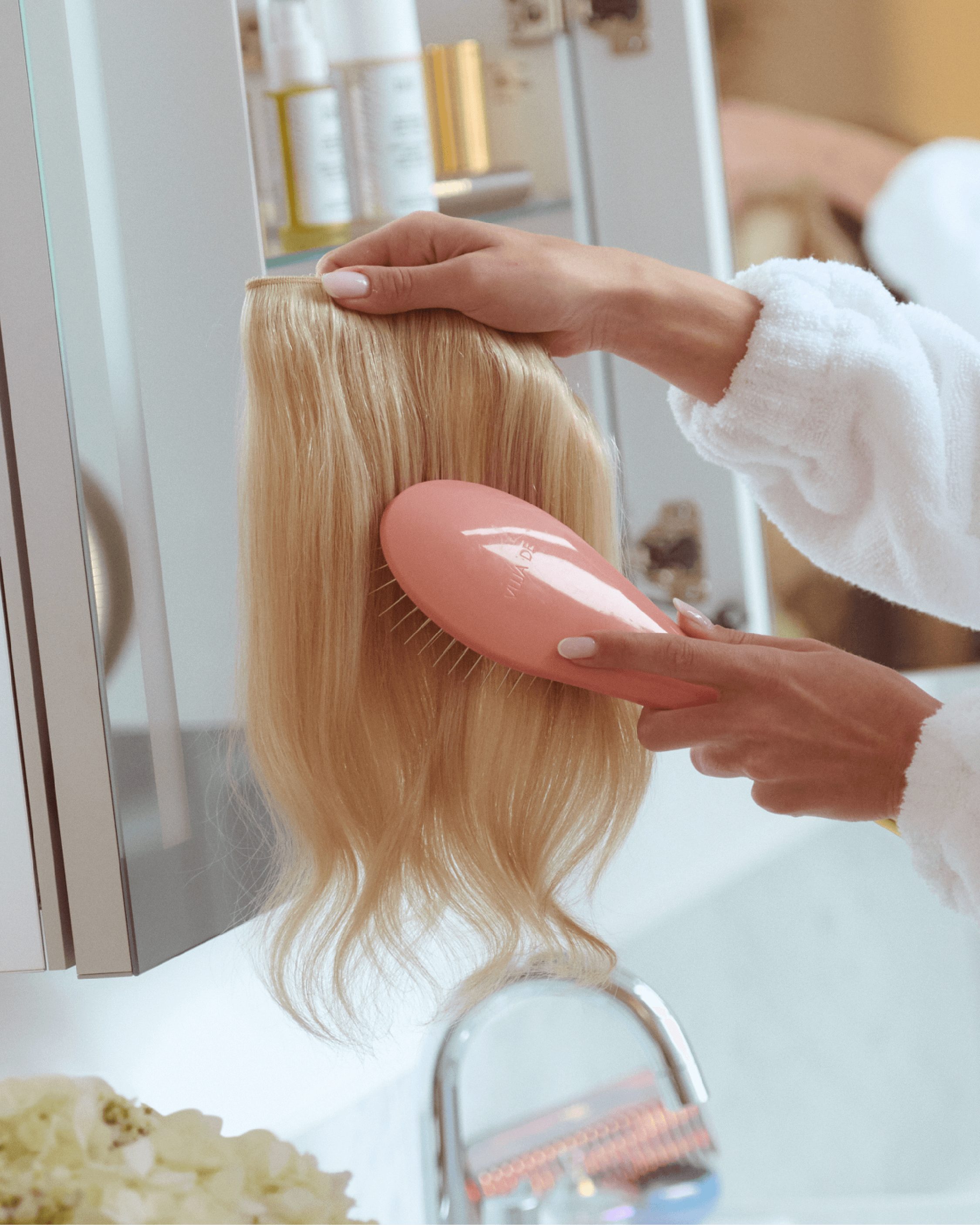 A woman brushes out her halo hair extension in her bathroom